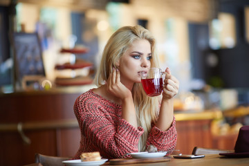 Young fashion woman drinks tea a cafe. caucasian woman sitting in act to drink a cup of tea