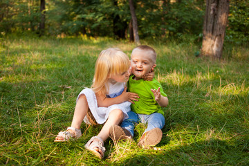 Naklejka na ściany i meble Little girl hugging little boy and playing, outdoors in summer