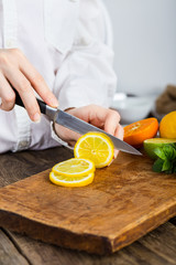 young clean chef hands cutting lemon on old wooden table in kitchen