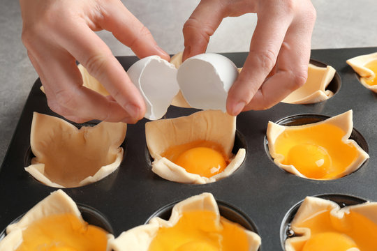 Woman adding egg to baking mold with dough, closeup