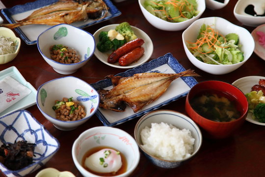 Japanese ryokan breakfast dishes including cooked white rice, grilled fish, boiled egg, miso soup,  natto, other side dishes
