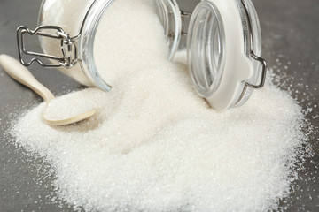 White refined sugar scattered from jar on grey table