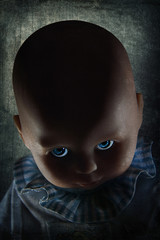 Creepy looking doll with blue eyes with dramatic lighting and textured background.