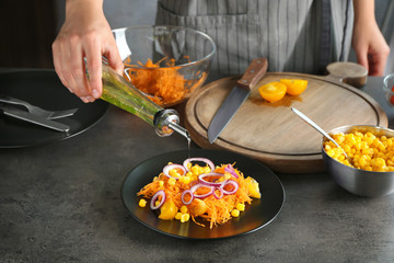 Woman pouring oil on carrot salad in kitchen