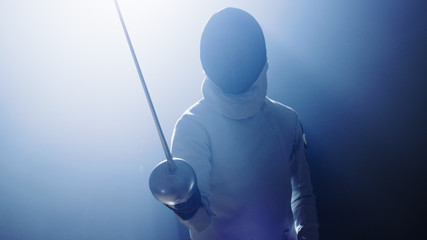 Fully Equipped Fencer Puts Lifts Foil Sword in Readiness for a Match. He Stands in the Spotlight...
