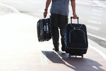 rear view of a man with a suitcase and a bag, walking on a sidewalk