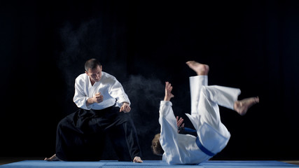 Martial Arts Master Wearing Hakamas Teaches Young Student Aikido Technique of Throwing over the Shoulder Shot Isolated on Black Background. - obrazy, fototapety, plakaty