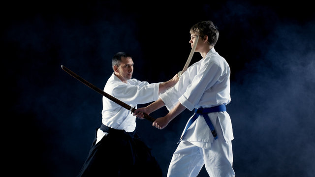 Martial Arts Master Teaches His Young Student How to Fight with Wooden Sword Bokken. Sparring ends in Seconds, Master Wins. Shot is Isolated on the Black Background.