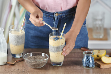 Young woman preparing smoothie with chia seeds on table in kitchen