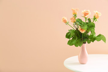 Bouquet of apricot roses in vase on table against trendy color background