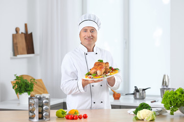 Male chef holding plate with cooked chicken and vegetables in kitchen