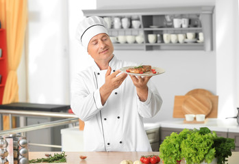 Male chef holding plate with cooked meat in kitchen