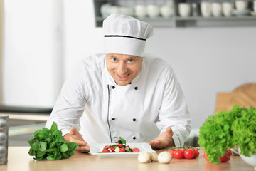 Male chef in uniform with salad on kitchen table