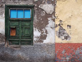 detail of empty derelict small house with decaying bricks broken plaster and green window with fading colors