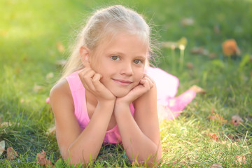 Naklejka na ściany i meble Cute little girl lying on green grass in park