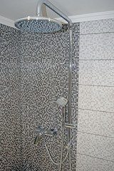 Chrome massage shower head and rail on grey square tiles background