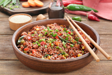 Bowl with brown rice and vegetables on wooden table, closeup