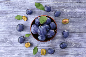 Bowl with ripe plums on wooden background