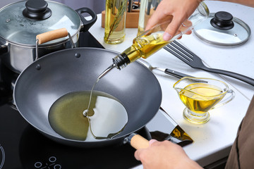 Man pouring cooking oil from bottle into frying pan on stove