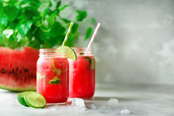 Fresh red watermelon slice and smoothie in glass jar with straw, ice, mint, lime on light...