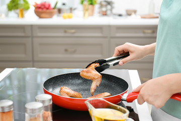 Woman cooking chicken wings in frying pan on stove