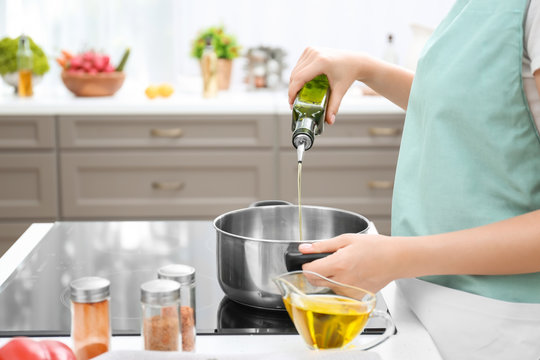 Woman pouring cooking oil from bottle into saucepan on stove