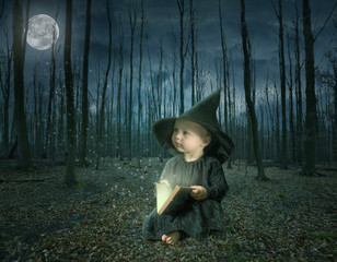 little halloween witch reading a magic book in a fairy tale forest