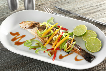 Serving plate with delicious fish in sauce and vegetables on wooden table, closeup