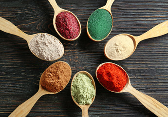 Different colorful superfood powders in spoons on wooden table