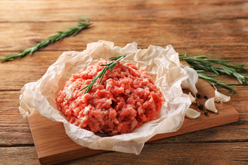 Parchment paper with fresh minced meat on wooden board