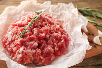 Parchment paper with fresh minced meat on wooden board