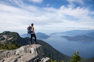 Obraz premium Wysportowany i żądny przygód mężczyzna z Ameryki Łacińskiej wędruje po grzbiecie górskim z pięknym widokiem na ocean w tle. Zrobiono w Lions Peaks, na północ od Vancouver, Kolumbia Brytyjska, Kanada.