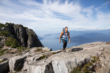 Fit and Adventurous Latin American man is hiking on top of a mountain ridge with a beautiful ocean view in the background. Taken at Lions Peaks, North of Vancouver, British Columbia, Canada.
