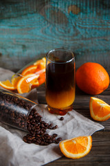 Layered non-alcoholic cocktail recipe idea. Orange juice in the bottom and dark coffee on the top in the glass. Bright and cozy still life of coffee beans, orange slices and layered cocktail.