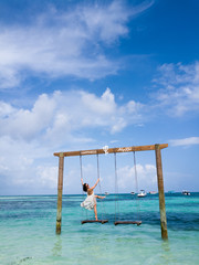 lady with beach dress poses on the swing at the beach