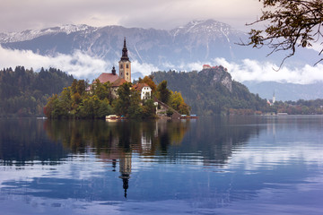 Autumn view of  the historical church on the island in Lake Bled in front of snow capped mountains under clouds