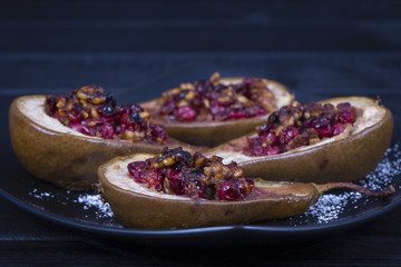 Homemade baked pears with honey, red cranberries and walnuts in black plate, close up