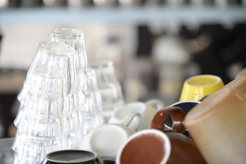 many glasses and coffee cups stacked on shelf in coffee shop.