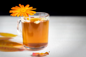 Cup of tea with petals, autumn leaves on a white wooden background. Black backdrop.
