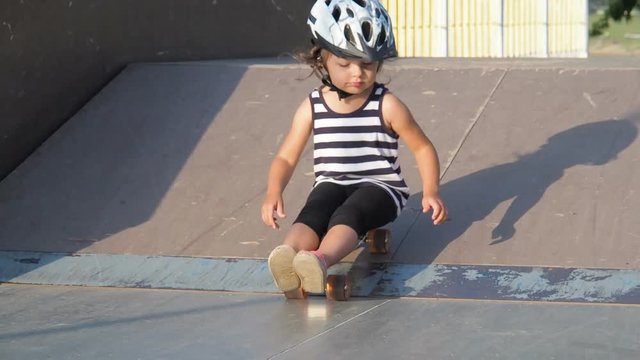 Little girl sitting on a skateboard. The child is riding on wheels.