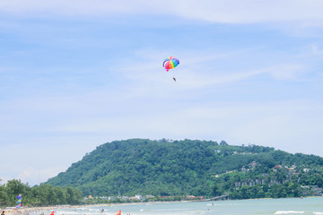 Parachute floats in the sky above the green mountains.