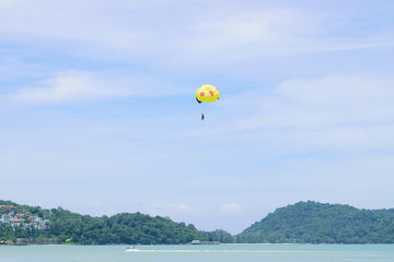 Parachute floats in the sky above the green mountains.