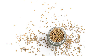 Organic Dried coriander seeds (Coriandrum sativum) in a glass jar, selective focus, on white background