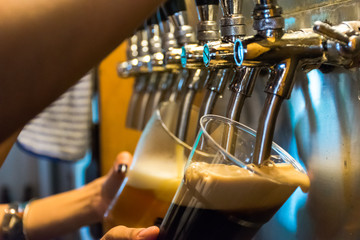 Close-up of bartender hand at beer tap pouring a lager beer in a glass.Craft beer poured into a pint glass.