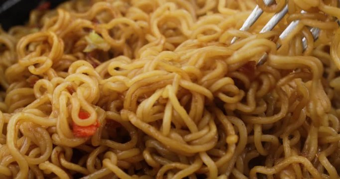 Close video of eating beef flavored ramen noodles with a fork in a black microwavable tray.