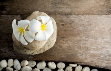 Fototapeta na wymiar White flower and leafs with big and tiny stone and towel on wood table for health spa advertisement and presentation