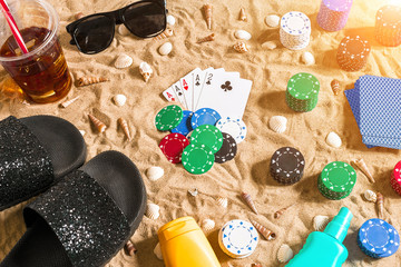 Gambling on vacation concept - white sand with seashells , colored poker chips and cards. Top view