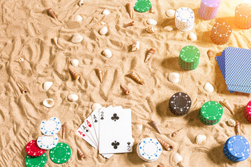 Fototapeta na wymiar Gambling on vacation concept - white sand with seashells , colored poker chips and cards. Top view