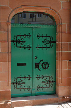 Alte grüne hölzerne Doppeltür mit schwarzem schmiedeeisernem Zierbeschlag in einer Sandsteinfassade