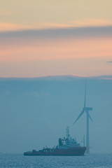 Soft image of a misty morning at sea. Sunrise with ship and turbine from offshore wind farm